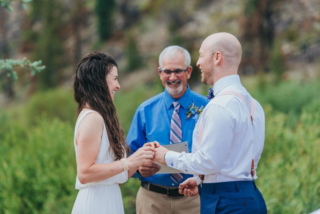 Mountain bride laughs as she puts ring on groom's finger in outdoor Colorado wedding
