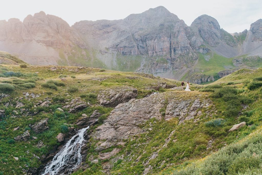 Bride and groom eloping walk by waterfall in Colorado mountains