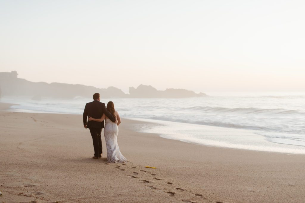 Bride and groom walk on foggy beach