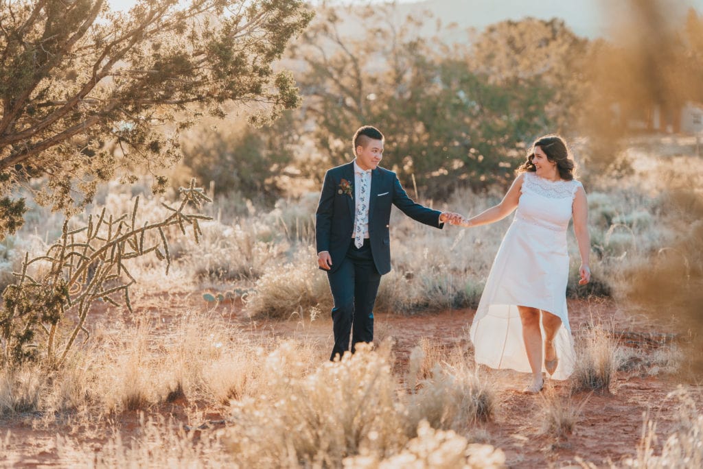LGBTQ couple walks through desert scrub in golden light at their elopement