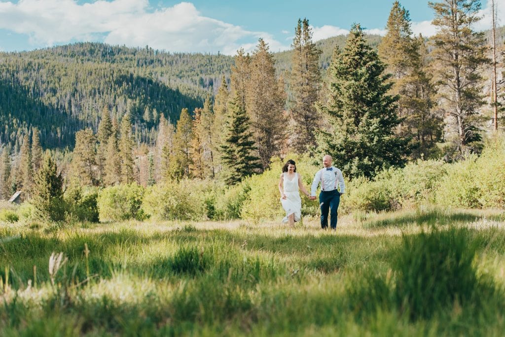 Wedding couple runs through meadow by Breckenridge, Colorado mountains
