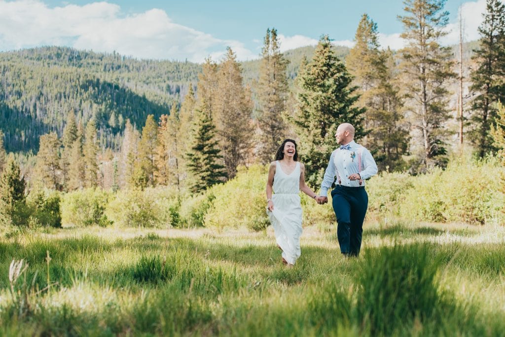 Bride and groom laugh as they run through a field by Breckenridge, Colorado mountain