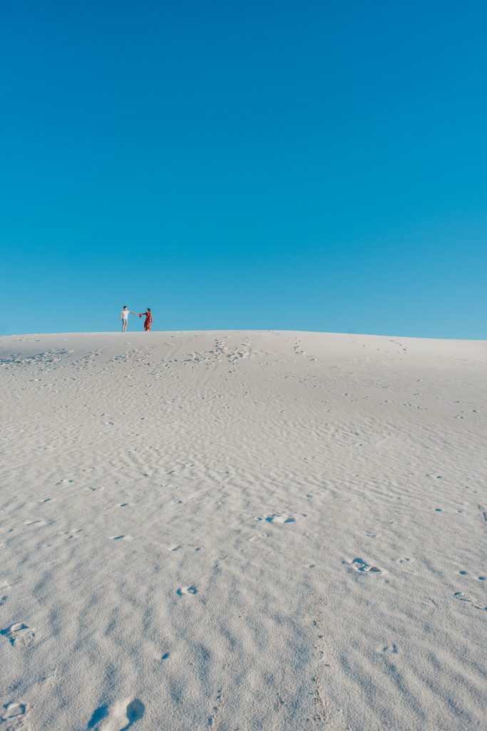 Couple walks across ridge of a white sand dune