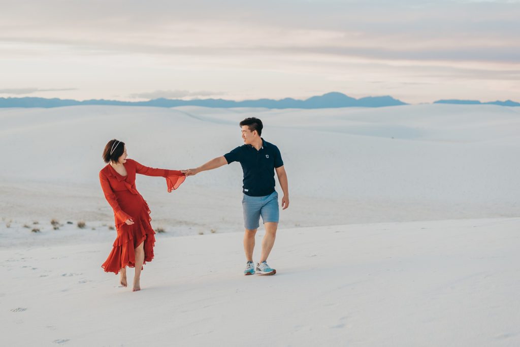 Couple holds hands and walks across dune at White Sands
