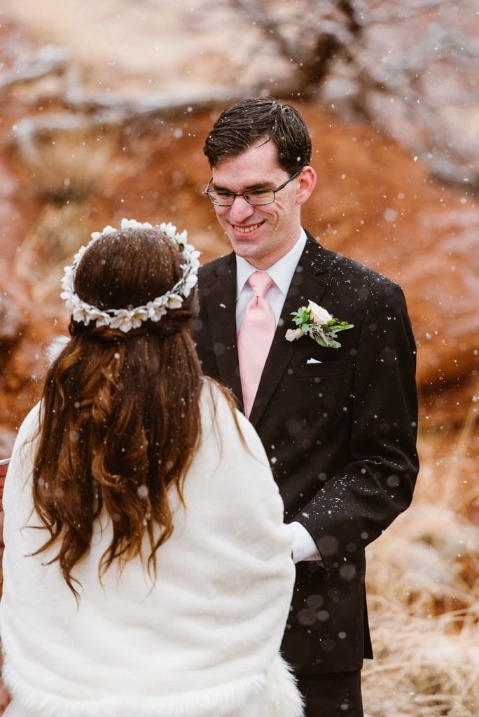 Groom looks lovingly at bride as she says her vows with snow falling