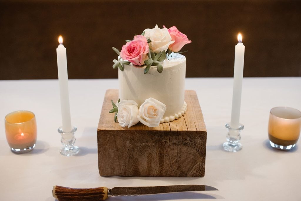 Small elopement cake with succulents and roses on a rustic wood block with candles.