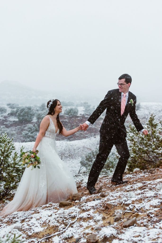 Couple hikes up a hill in the red rocks of Desert Harbor Retreat for their elopement