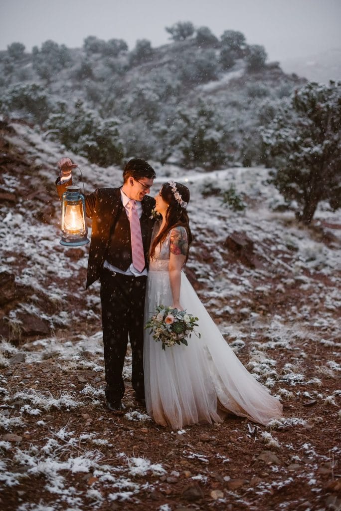 A couple looks lovingly at each other by the light of a lantern while standing in the snow