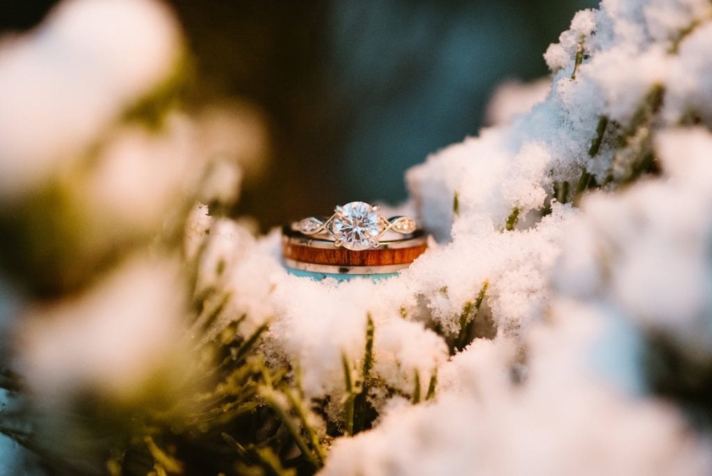A bride's diamond ring and a groom's unique wood and turquoise inlaid wedding ring sit in the snow