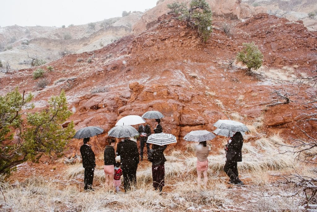 Family gathers for red rock elopement ceremony in the snow with umbrellas.